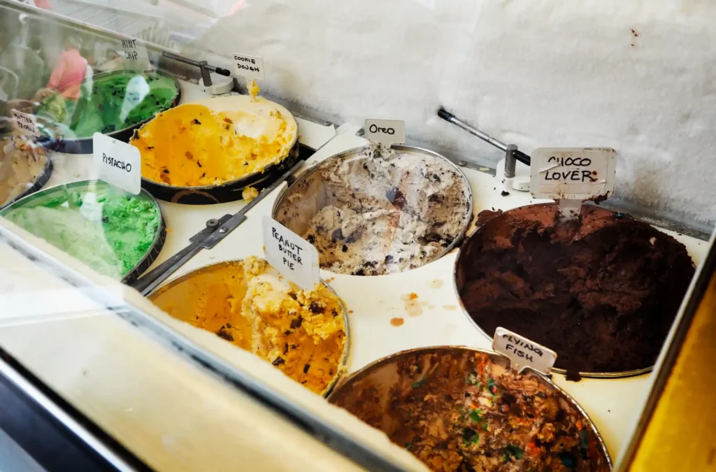 Sorveteria self service por quilo: vitrine com potes de sabores de sorvete expostos, placas de identificação e bandejas em layout de autoatendimento para servir e pesar.