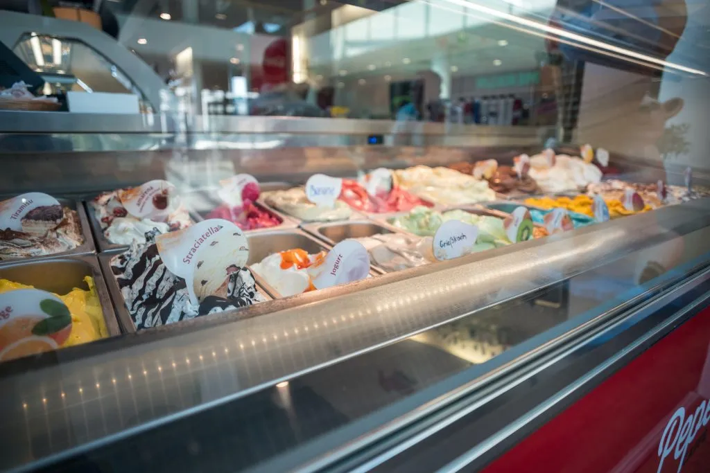 Na imagem, podemos observar uma vitrine de sorveteria com diversos sabores em exibição